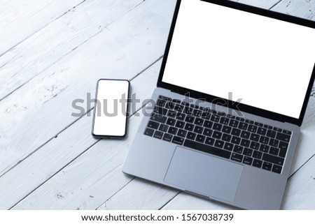 The Laptop and phone with blank screens on white wooden table. Workspace. Copy space
