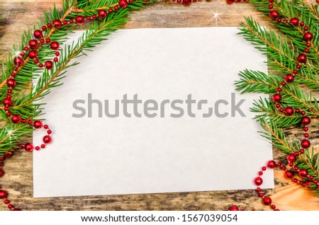 White leaf on wooden background with Christmas tree branches and red beads close up with copy space. Beautiful Christmas background or greeting card