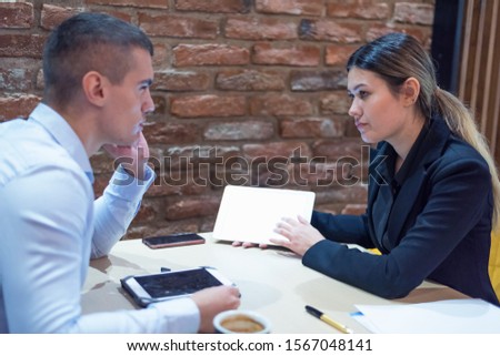 Two young male and female multiracial business people working connected with technological devices at the bar. Two young creative coworkers working with new startup project.