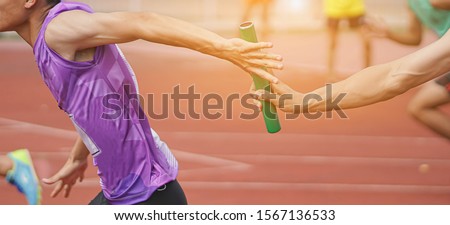 Professional Athlete passing a baton to the partner against race on racetrack.selective focus. Royalty-Free Stock Photo #1567136533
