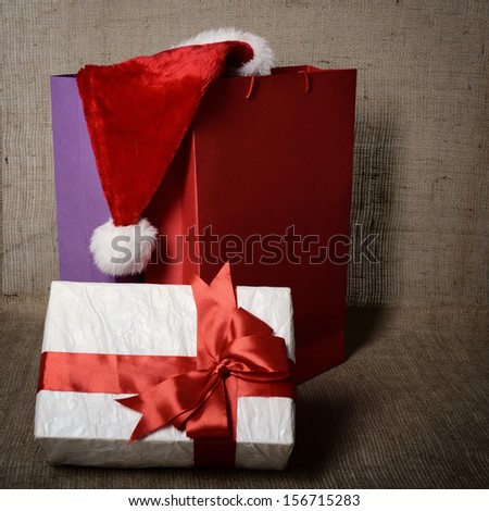 ?hristmas gift box with colored bags and Santa's hat over canvas background, holiday shopping concept