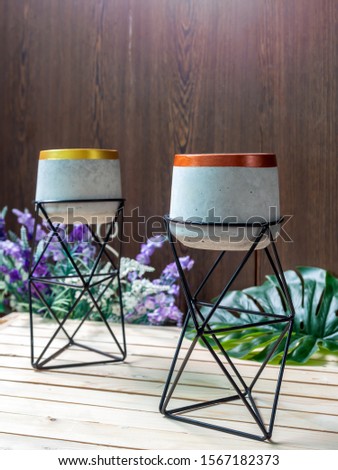 Cactus pot. Concrete pot with iron stand. Empty modern standing planter with flower and palm leaf on wooden table on wooden background vertical style.