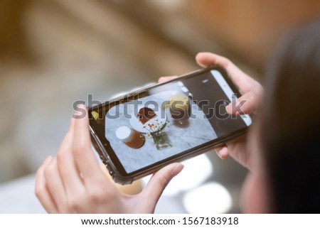 A girl take a picture of coffee and cake by smartphone in cafe 