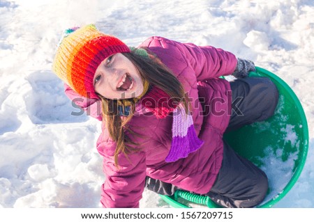 A child rolls down a snowy hill. Emotion girl on a walk. Winter holiday. Outdoor games. Warm clothes cozy hat in cold weather on the street
