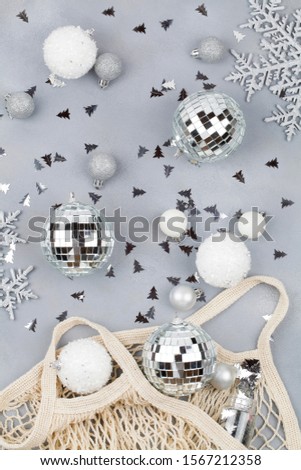 Xmas holiday decorative white and silver balls and snowflakes flowing from eco-friendly shopping mesh bag on blue background. top view flat lay close up