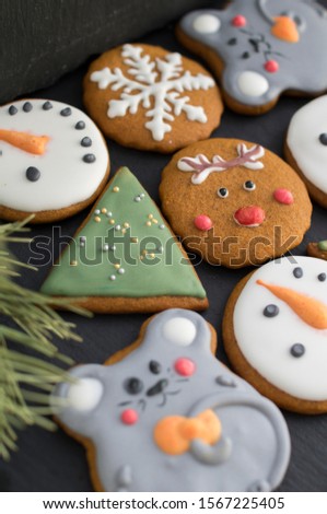 set of Christmas gingerbread cookies (snowman, deer, tree, mouse, snowflake) on a black background with a blurry fir branch