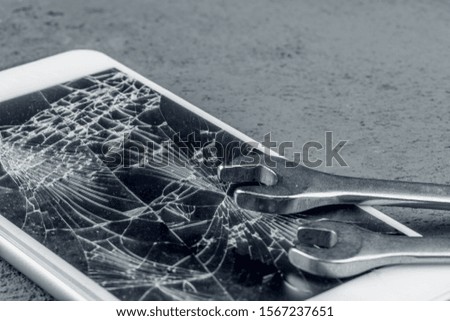 Crashed smartphone with repairing tools on grey background