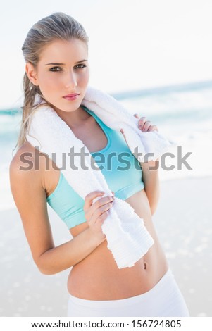 Relaxed fit blonde in sportswear on a sunny beach holding towel