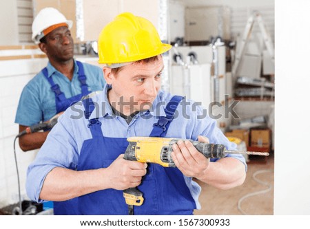 Focused builder handyman working with electric drill indoors
