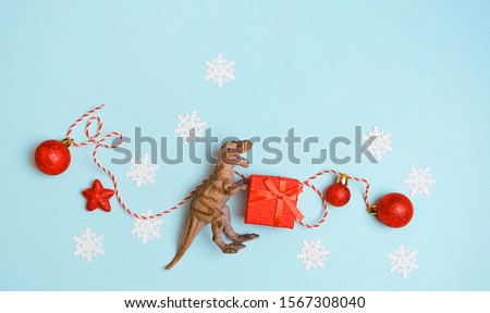 Dinosaur toy with gift box, Christmas red balls. Christmas and New Year holiday. T-rex and winter decor on blue background. Funny party. winter festive creative concept