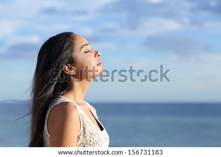 Profile of a beautiful arab woman breathing fresh air in the beach with a cloudy blue sky in the background