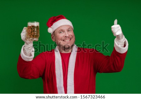 Emotional male actor in a costume of Santa Claus holds a glass of beer in his hands and poses on a green chrome background
