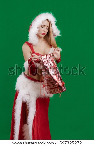 Beautiful emotional young girl with long hair dressed as Santa Claus with a Christmas bag for gifts in hands posing on a green chrome background