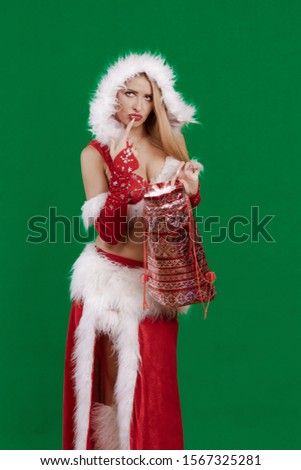 Beautiful emotional young girl with long hair dressed as Santa Claus with a Christmas bag for gifts in hands posing on a green chrome background