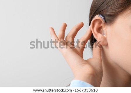 Young woman with hearing aid on light background Royalty-Free Stock Photo #1567333618