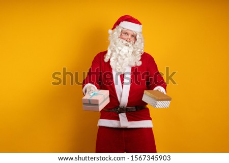 Male actor in a costume of Santa Claus holds two gift boxes in his hands and poses on a yellow background