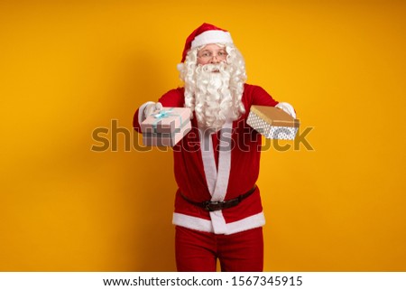 Male actor in a costume of Santa Claus holds two gift boxes in his hands and poses on a yellow background