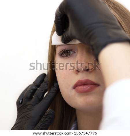 Female cosmetologist performs eyebrow correction on beautiful models in the beauty parlor. Fair-haired girl. Close-up. Facial care