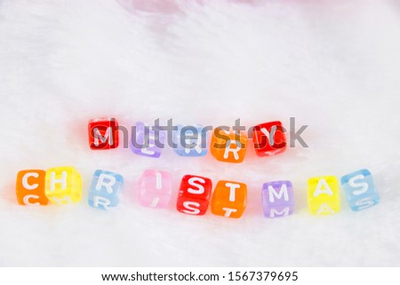 Merry Christmas composed of small multicolored letters on the surface of white and fluffy background, selective focus