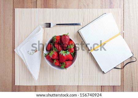 Bowl of fresh strawberries with a notebook for recipes