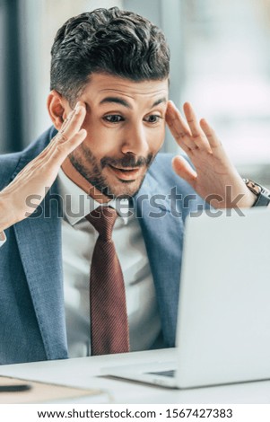 excited businessman showing wow gesture while looking at laptop