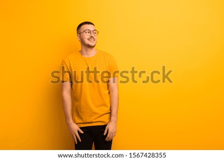 young handsome man feeling shocked, happy, amazed and surprised, looking to the side with open mouth against flat background