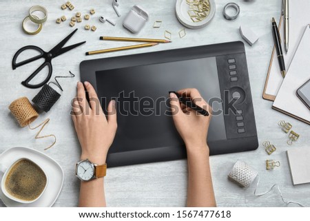 Female designer working with graphics tablet at white table, top view