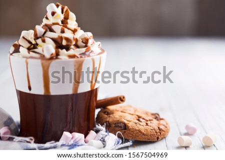 A messy cup with hot chocolate, whipped cream, marshmallows and chocolate chip cookies.