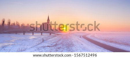 A church in a frozen winter landscape in The Netherlands. Photographed at sunrise on a beautiful foggy morning.