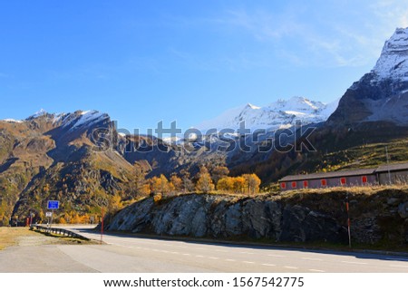 Mountain road with a beautiful autumn in Simplon pass with golden larch forest, snow mountain and blue sky background.