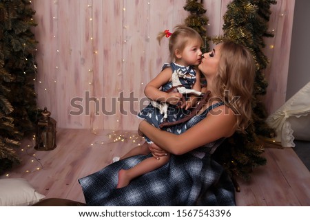 Smiling joyful mom with her daughter near the Christmas tree New Year, Christmas concept kiss