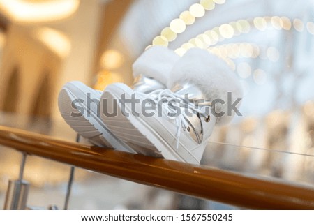 female white and silver winter ankle boots with fur on a thick sole on a blurred background of a shopping center. Shop womens shoes advertising