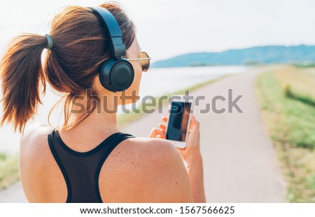 Young teenager girl starting jogging and listening to music using smartphone and wireless headphones. Active sport life concept image.