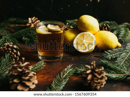 Glass of tea with lemon fruit lemons with fir branches and fir cones over a rustic background