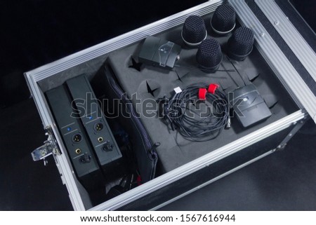 Various microphones; Dynamic, Dynamic wireless, clip-on condenser wireless microphones, and signal transmitter + receiver inside metal box hard case with grey foam. high angle closeup shoot.