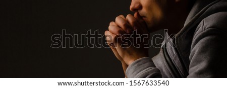 Religious young man praying to God on dark background, black and white effect Royalty-Free Stock Photo #1567633540