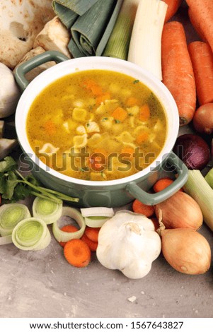 Broth with noodle and carrots, onions various fresh vegetables in a pot - colorful fresh clear spring soup. Rural kitchen scenery vegetarian bouillon or stock