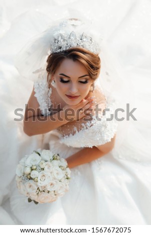 Bride with bouquet of flowers. Hair style bride with diadem, with beautiful earrings and lush white dress on your wedding day. Tender bride with  with closed makeup eyes. Top view