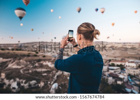 Man taking photo of beautiful landscape and balloons in Cappadocia with mobile camera, dreamy travel concept.