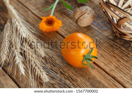 Close-up yellow tomato, walnuts, wheat ear, calendula flower and wicker basket on old wooden boards. Shallow depth of field. Top view.