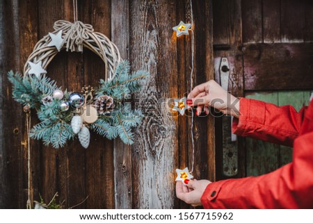Rear view young female hipsters decorate home for Christmas door outside. Beautiful Christmas tree wreath old wooden rustic background. girl red jacket and a striped hat and scarf. New year 2020