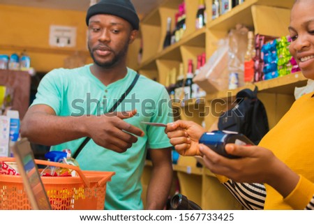 Black man making a card payment for the goods he bought in the supermarket from a beautiful woman
