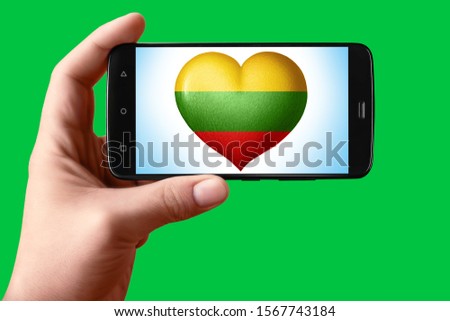 Lithuania flag in the shape of a heart on the phone screen. Smartphone in hand shows the heart of the flag on the background hromakey. Object for installation and design.