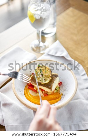 Roasted Halibut with vegetables, paprika pepper and pumpkin cream. Lunch in a restaurant, a woman eats delicious and healthy food. Dish decorated with a slice of lemon. Restaurant menu