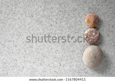 Gray artificial granite background decorated with a simple round granite pebble, placed in the right side. With copy space for text. Three stones zen buhddism pattern.