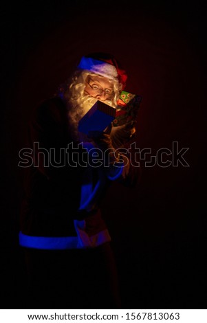 Male actor dressed as Santa Claus holds a gift box in his hands, looks into it and poses on a yellow background