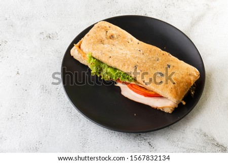 Baguette sandwich with salami, turkey breast, cheese, lettuce, tomatoes and onion on a cutting board. Long subway sandwiches isolated on white marble background. Homemade food. Tasty breakfast