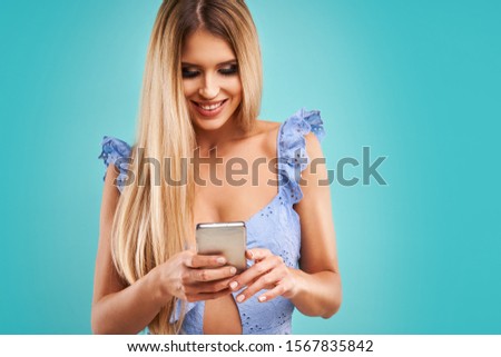Beautiful adult woman posing over blue background and using smartphone