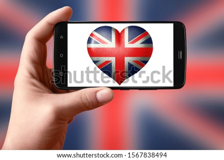 Britain flag in the shape of a heart on the phone screen. Smartphone in hand shows a heart flag. Mobile photography.