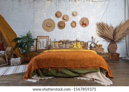 Beautiful cozy bedroom with boho style interior, pillows, cushions, green plants in flower pot, bed and house decor on night table and wall Royalty-Free Stock Photo #1567859371